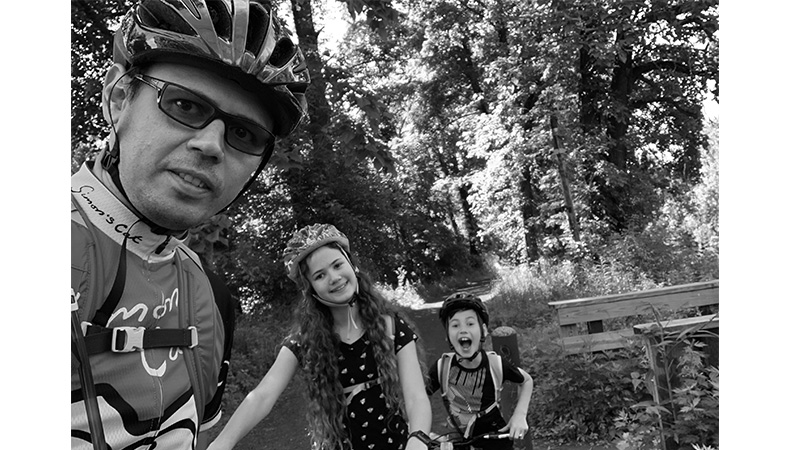 Oleg and his daughter and son with their bike gear on standing on a dirt trail with their bikes