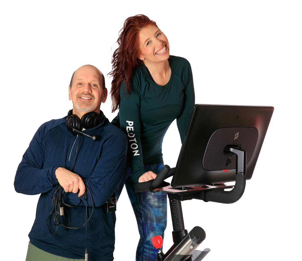 Peloton News podcast hosts Tom and Crystal O'Keefe pose near the Peloton Bike.