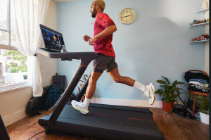 Peloton Tread in a living room setting with a runner in a red shirt, black shorts and white shoes