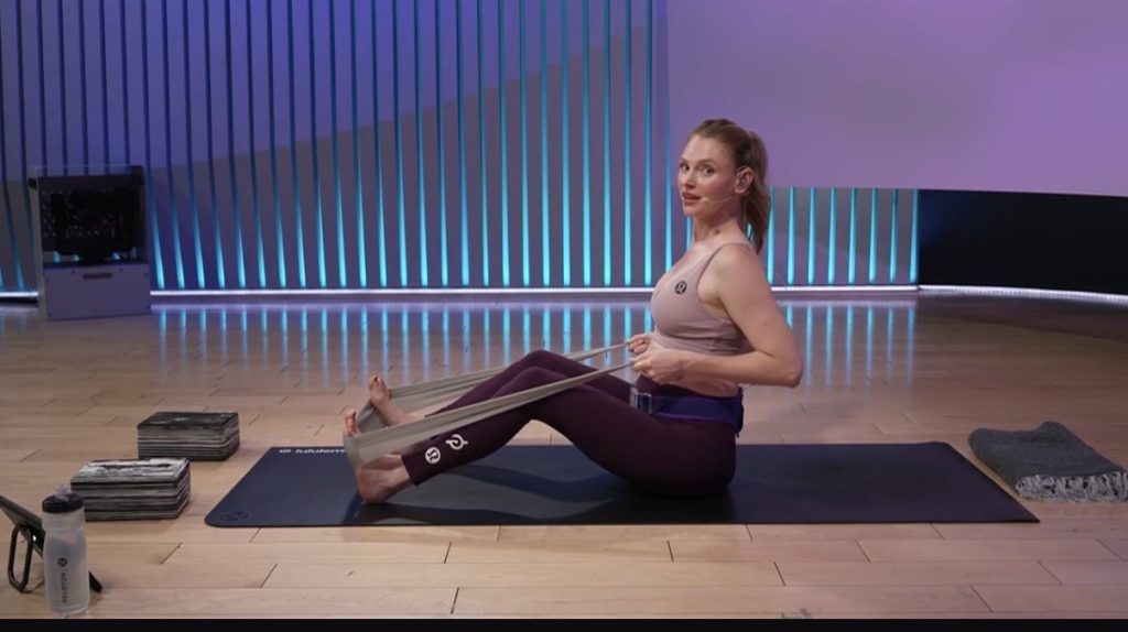 Prenatal Yoga + Pilates class using a resistance band during a seated seated stretch.