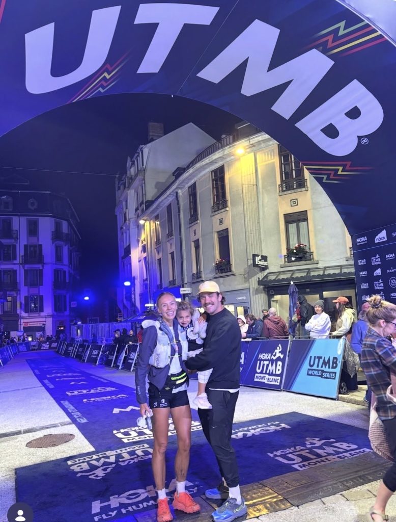 Becs Gentry CCC finish, standing under the UTMB arch with Austin Curtis and their child
