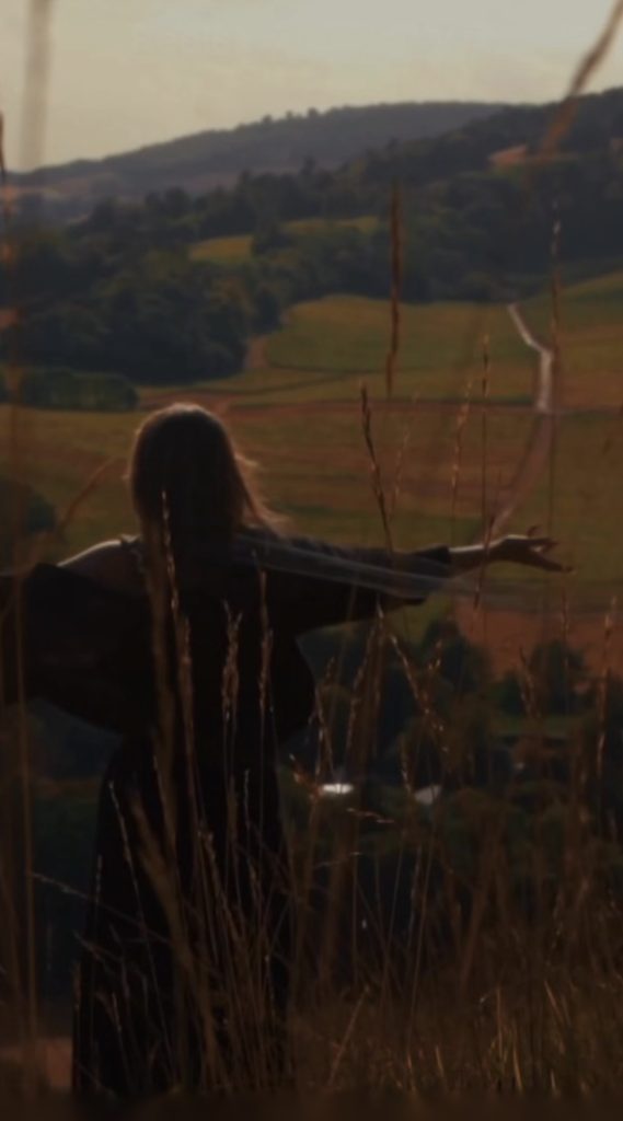 Jessie Malone stands in a field in a scene from her new music video