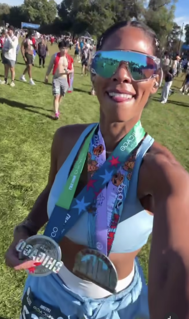 Kirsten Ferguson smiles in mirrored sunglasses while holding a Chicago finisher medal after the Chicago Half Marathon.